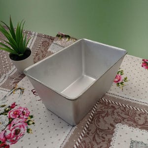 May include: A silver rectangular loaf pan with a smooth, shiny surface. The pan is empty and ready for baking.
