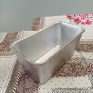 Puede incluir: Un molde para pan de plata, un molde para hornear rectangular con una superficie lisa y brillante. El molde está vacío y parece ser de metal.