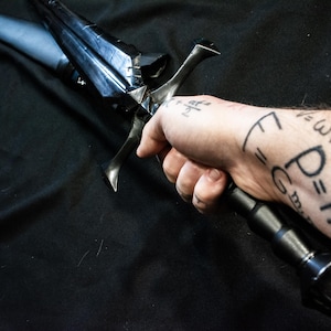 Puede incluir: Una espada negra con una hoja oscura y angular y un mango negro. La espada se sostiene en una mano con ecuaciones matem&aacute;ticas tatuadas en el brazo. El dise&ntilde;o de la espada sugiere un tema de fantas&iacute;a o hist&oacute;rico.