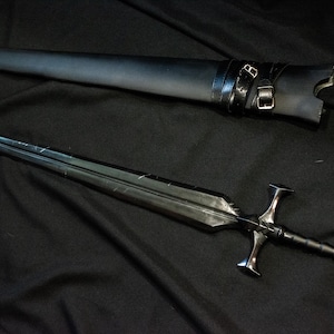 Puede incluir: Una espada negra con una hoja de doble filo y una empu&ntilde;adura en forma de cruz, sobre una superficie negra. La espada va acompa&ntilde;ada de una vaina de cuero negro con correas de hebilla. Tema medieval o fant&aacute;stico.