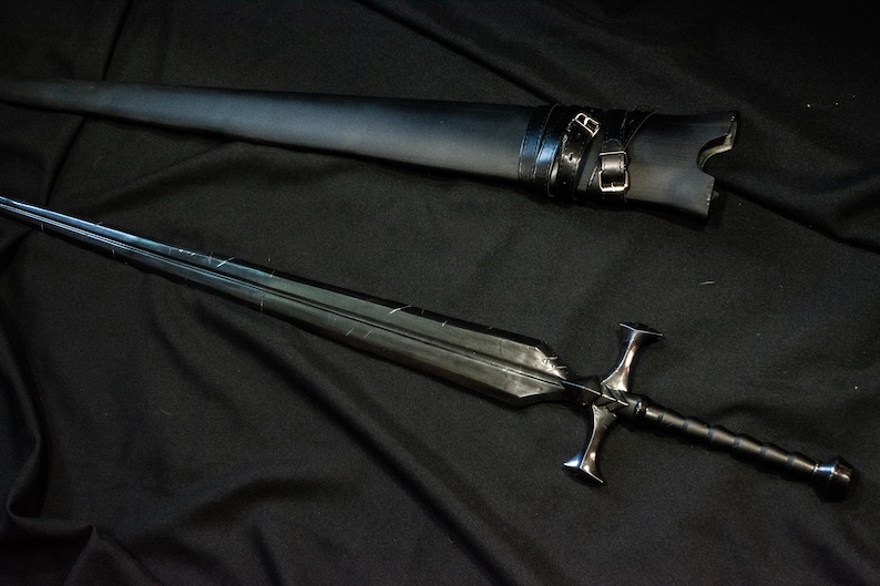 Puede incluir: Una espada negra con una hoja de doble filo y una empu&ntilde;adura en forma de cruz, sobre una superficie negra. La espada va acompa&ntilde;ada de una vaina de cuero negro con correas de hebilla. Tema medieval o fant&aacute;stico.