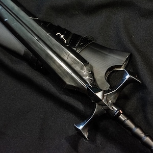 Puede incluir: Una espada negra con una guarda plateada y una hoja detallada. La espada tiene un mango oscuro y est&aacute; sobre un fondo negro. La hoja tiene dise&ntilde;os grabados y un peque&ntilde;o emblema.