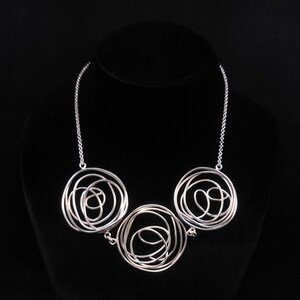 May include: A silver necklace with three circular pendants. Each pendant is made of a series of intertwined silver wires, creating a delicate and intricate design.