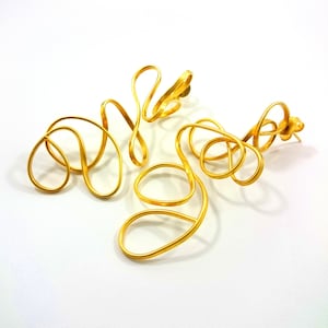 May include: A pair of gold-toned earrings with a unique, abstract design. The earrings are made of thin, twisted wire that forms a series of loops and curves.