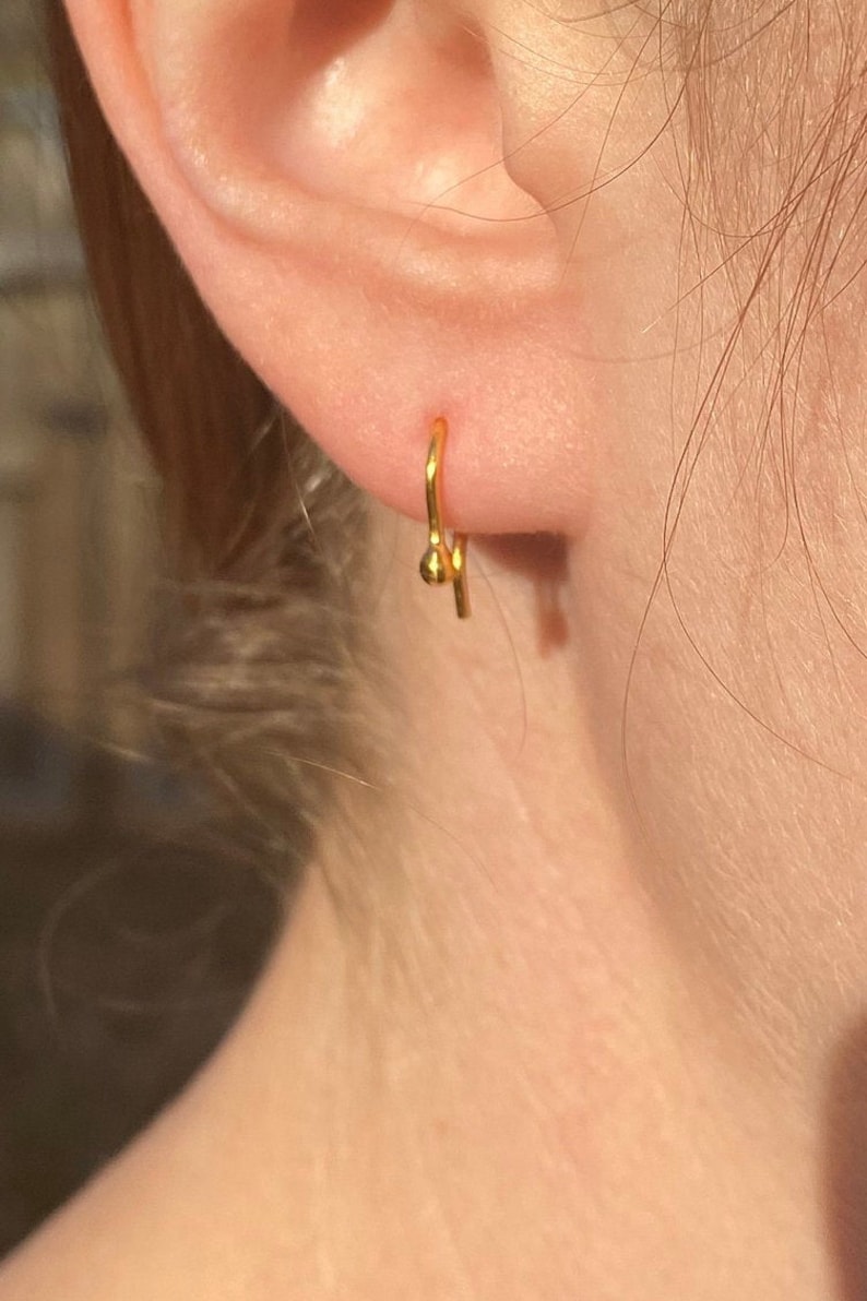 May include: A gold hoop earring with a small ball at the end.