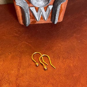 May include: Two gold-colored earring hooks with a small round ball at the end of each hook.
