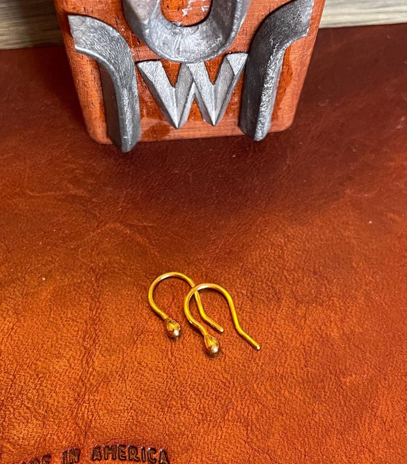May include: Two gold-colored earring hooks with a small round ball at the end of each hook.