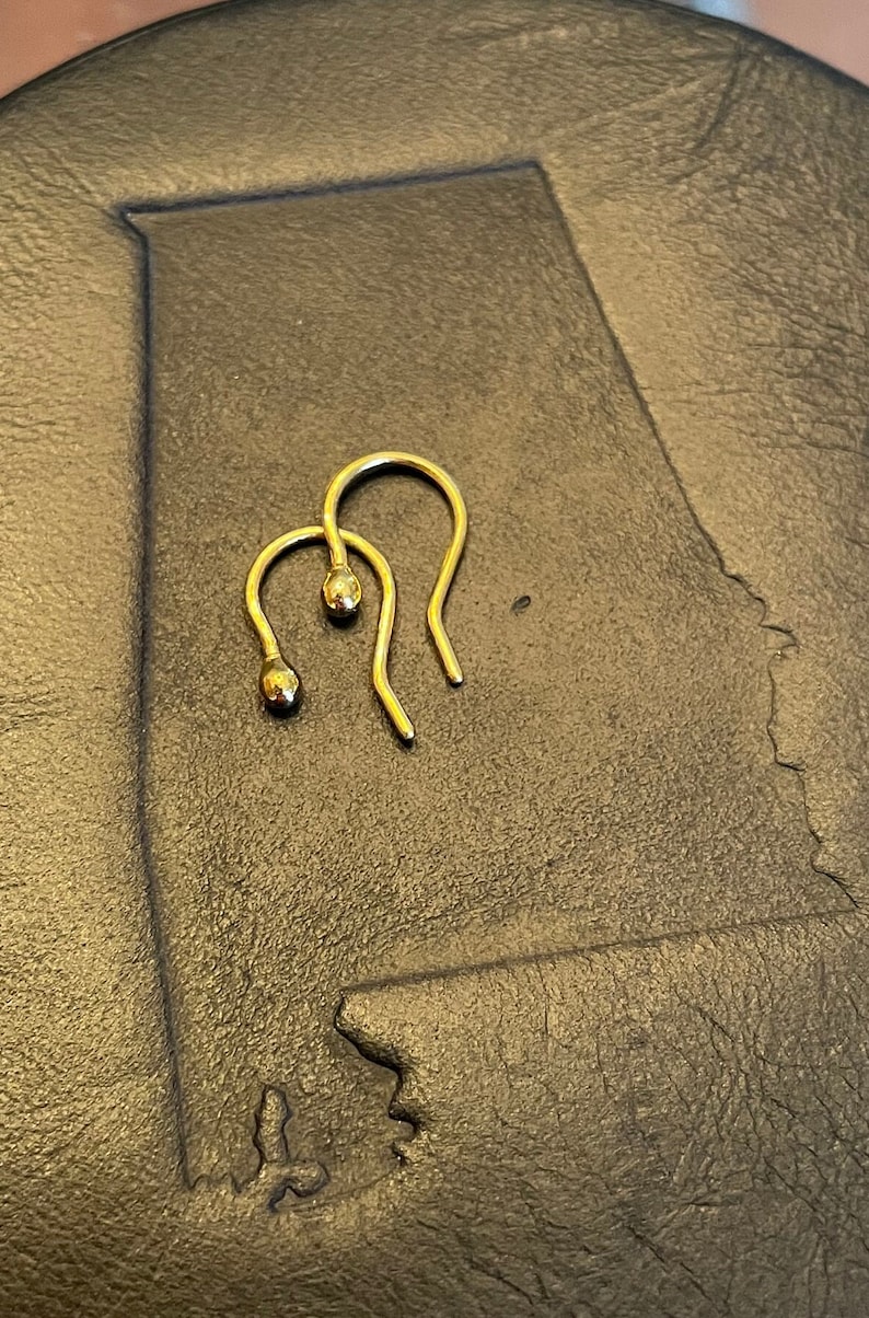 May include: A pair of gold hoop earrings with a small ball at the end of each hoop.