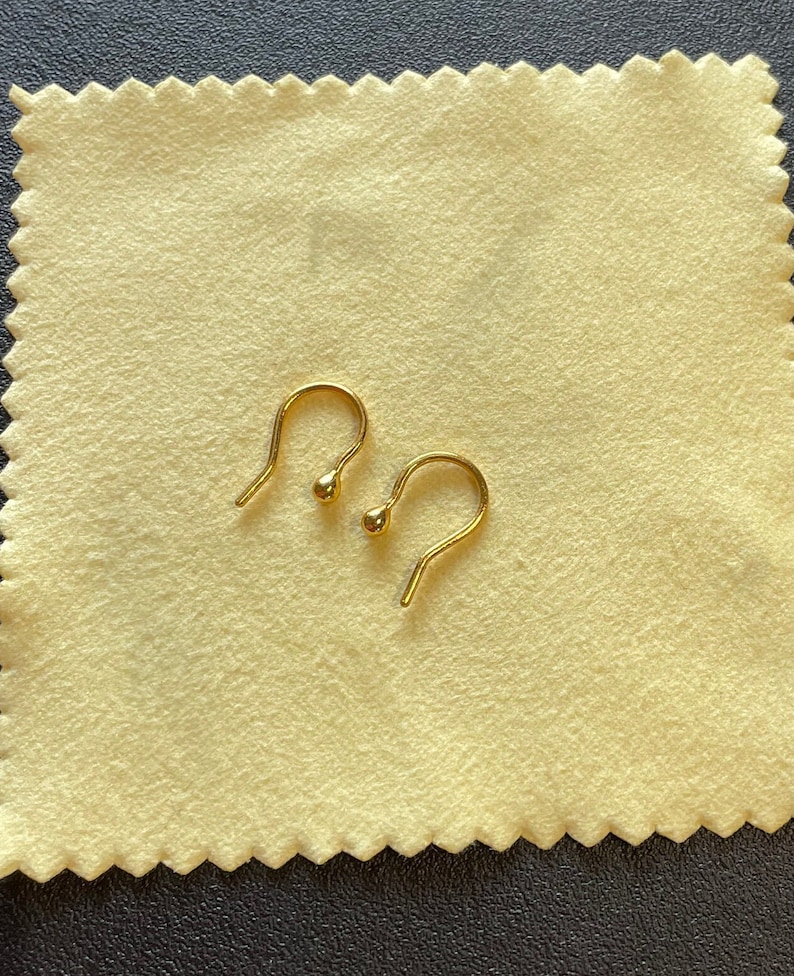 May include: Two gold-colored earring hooks with a small ball at the end of each hook.