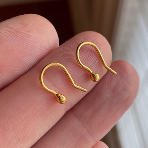 May include: A pair of gold hoop earrings with a small ball at the end of each hoop.