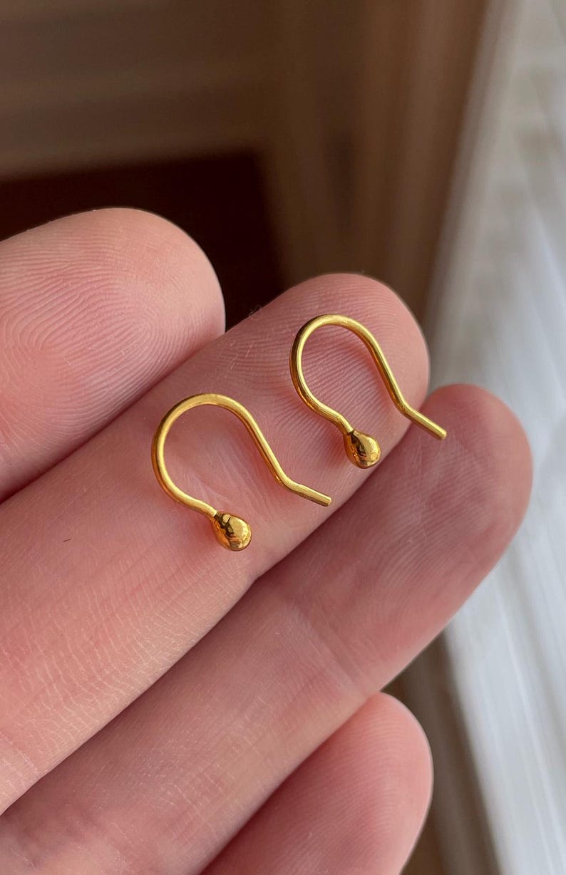 May include: A pair of gold hoop earrings with a small ball at the end of each hoop.