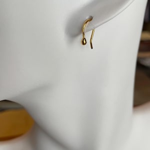 May include: A gold-toned earring with a small ball at the end of the hook.