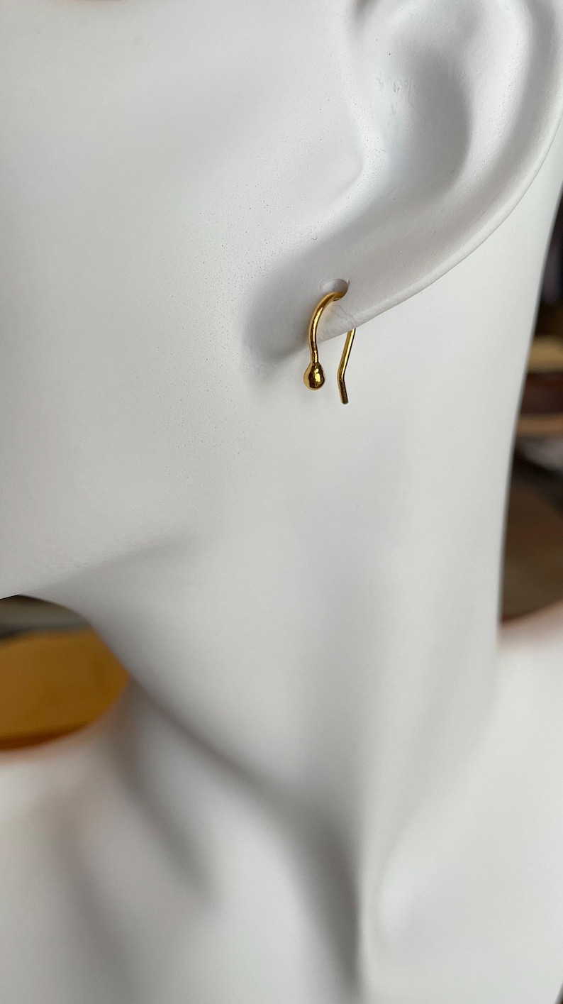 May include: A gold-toned earring with a small ball at the end of the hook.