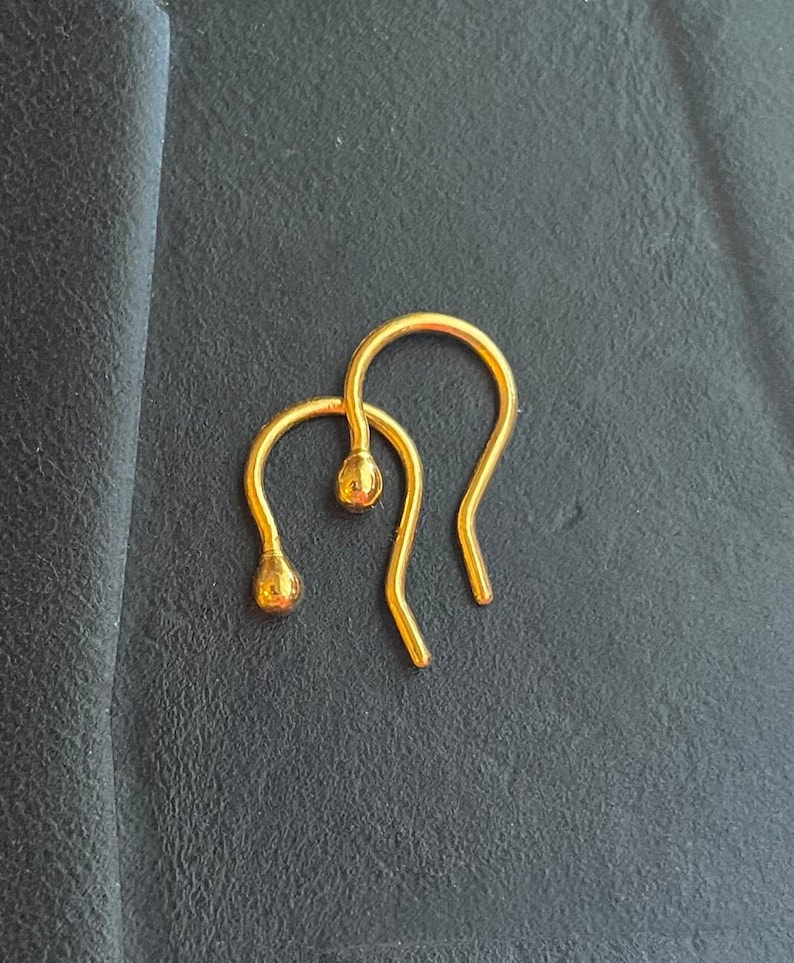 May include: Two gold earring hooks with a small round ball at the end of each hook