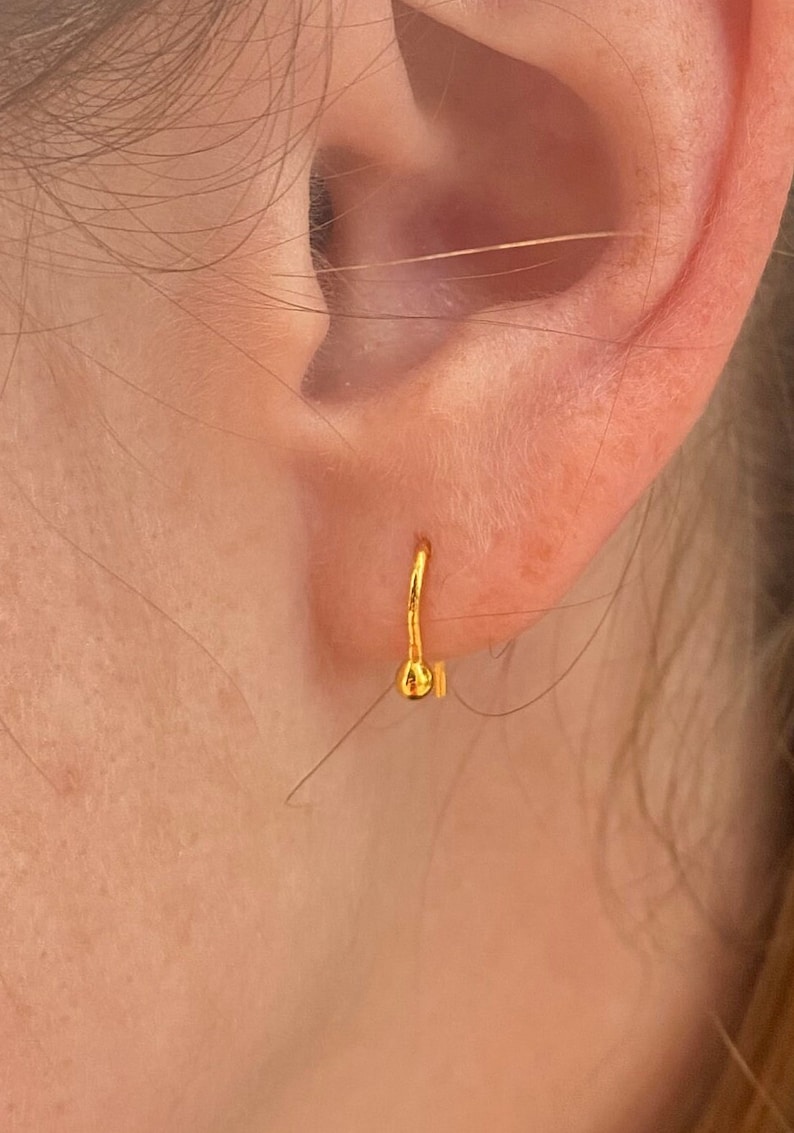 May include: A gold hoop earring with a small ball at the end. The earring is worn in the upper lobe of the ear.