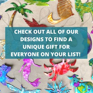 May include: A collection of colorful metal ornaments featuring various designs, including a palm tree, a hummingbird, a mermaid, a crab, a snowflake, and a cow. The ornaments are hanging from strings and are arranged on a brown surface. The text "CHECK OUT ALL OF OUR DESIGNS TO FIND A UNIQUE GIFT FOR EVERYONE ON YOUR LIST!" is displayed in a blue box.