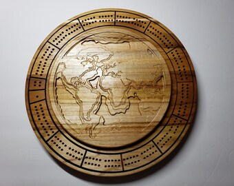 May include: A circular wooden cribbage board featuring a carved world map in the center. The outer ring contains drilled holes for scoring, arranged in sections separated by dark lines. The natural wood grain is visible throughout the board.