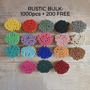 May include: A collection of colorful match bundles arranged on a wooden surface. The matches are in various colors, including yellow, red, green, purple, pink, blue, orange, and brown. The text "RUSTIC BULK - 1000pcs + 200 FREE" is at the top.
