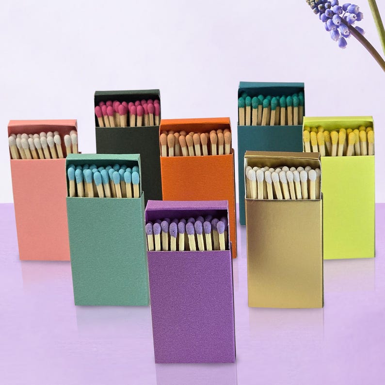 May include: Assortment of matchboxes in various colors, including pink, green, orange, gold, purple, and yellow. Each box contains a stack of matches with colored tips.