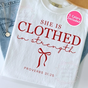 May include: A white t-shirt with the red text "SHE IS CLOTHED in strength" and "PROVERBS 31:25". A pink circle with "5 Colors Included" is on the shirt. The shirt is folded on top of blue jeans.