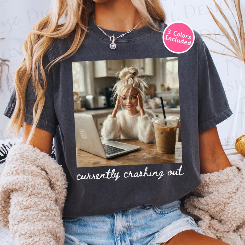 Peut inclure: T-shirt gris fonc&eacute; avec un graphisme d'une femme devant un ordinateur portable, un caf&eacute; et le texte "currently crashing out". Un cercle rose indique "3 couleurs incluses".