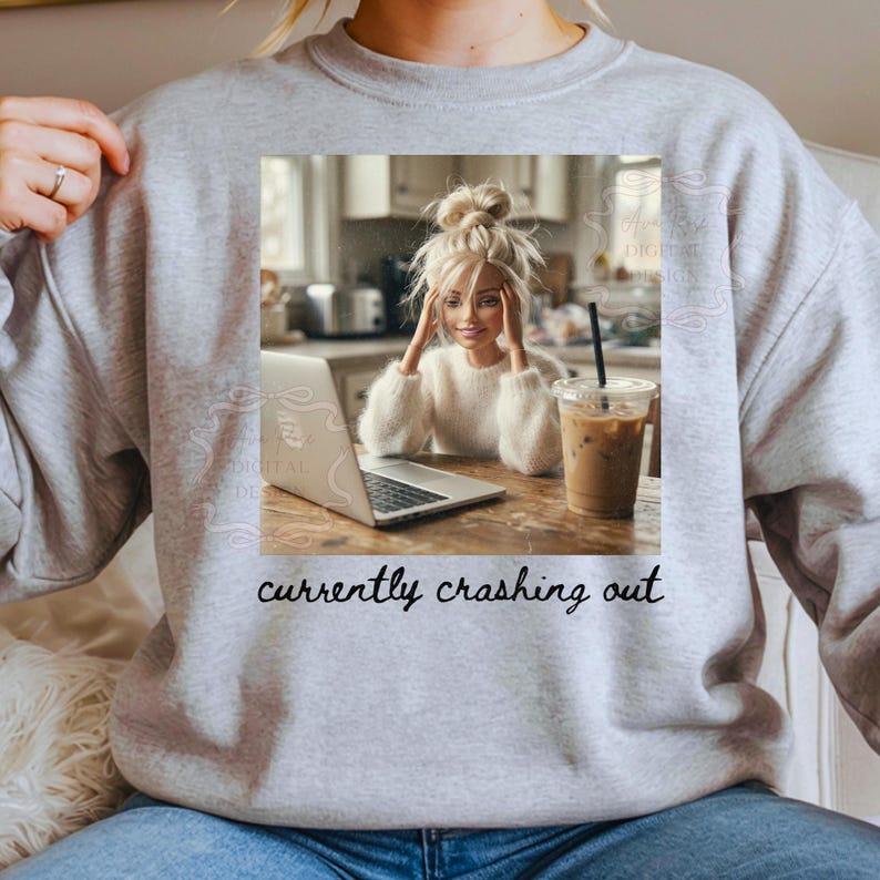 Peut inclure: Sweat-shirt gris avec une image imprim&eacute;e d'une femme avec un ordinateur portable et un caf&eacute; glac&eacute;. L'image contient le texte "currently crashing out" en &eacute;criture cursive.