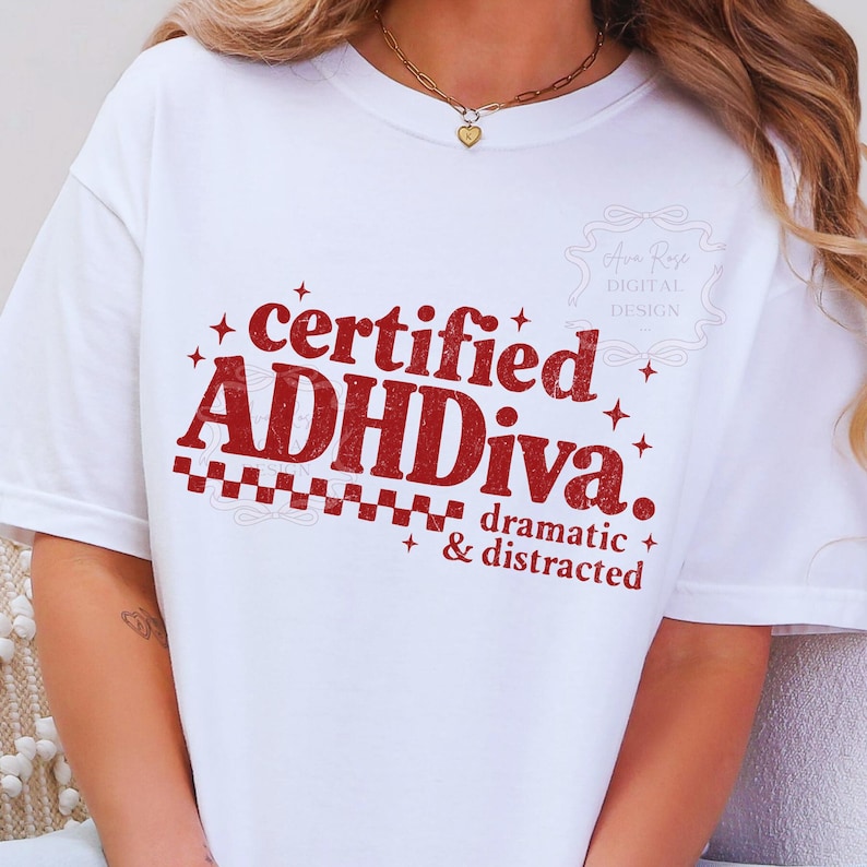 Pode incluir: Camiseta branca com o texto vermelho "certified ADHDiva. dramatic & distracted". O design inclui estrelas e um padr&atilde;o xadrez. Um colar de ouro com um pingente de cora&ccedil;&atilde;o &eacute; vis&iacute;vel.