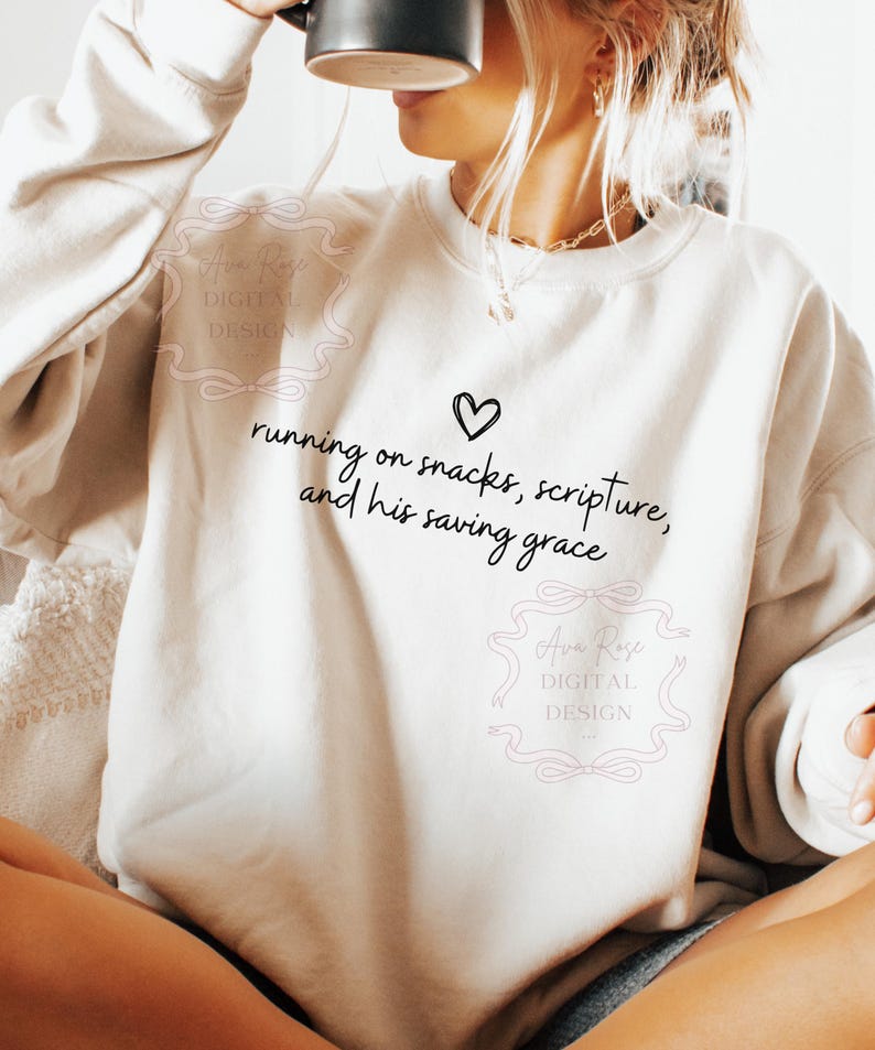 May include: Cream-colored sweatshirt with the text "running on snacks, scripture, and his saving grace" in black script, along with a heart symbol. The sweatshirt has a crew neck and long sleeves.