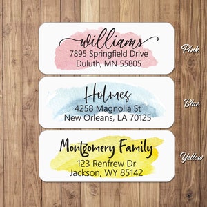 May include: Three watercolour address labels with different coloured backgrounds. The first label is pink with the text "Williams", "7895 Springfield Drive", "Duluth, MN 55805". The second label is blue with the text "Holmes", "4258 Magnolia St", "New Orleans, LA 70125". The third label is yellow with the text "Montgomery Family", "123 Renfrew Dr", "Jackson, WY 85142".