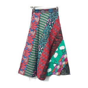 Op de afbeelding: Een kleurrijke patchwork rok met een bloemenprint. De rok is gemaakt van verschillende stoffen en heeft een verscheidenheid aan kleuren, waaronder rood, groen, blauw en zwart.
