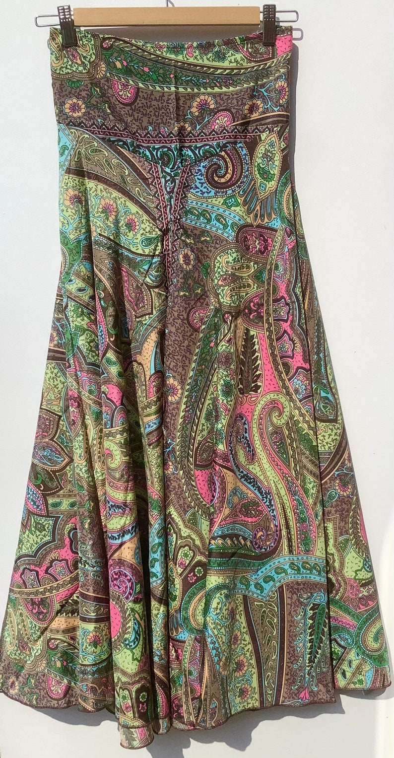 May include: A long, flowing skirt with a paisley print in shades of brown, green, pink, and blue. The skirt has a wide waistband and a flowing, A-line silhouette.