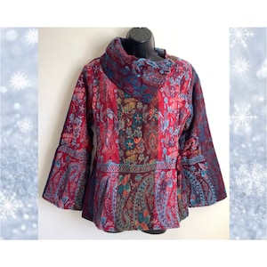 Peut inclure: Une blouse à manches longues avec un col roulé et des manches bouffantes, ornée d'un motif rouge, bleu et vert.