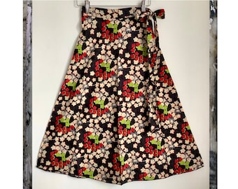 May include: A black wrap skirt with a floral print featuring red, white, and green flowers. The skirt has a tie closure at the waist.