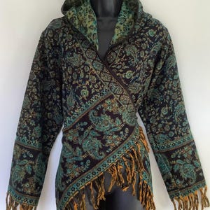 May include: A wrap jacket with a hood, featuring a paisley design in teal, gold, and black. The jacket has long sleeves and a fringed hem. The hood and lining are teal with a floral pattern. The jacket is displayed on a black mannequin.