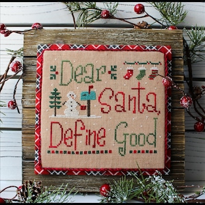 May include: A cross-stitch pattern framed in a wooden frame with a red and black plaid border. The pattern features a snowman standing next to a mailbox with the text "Dear Santa, Define Good".