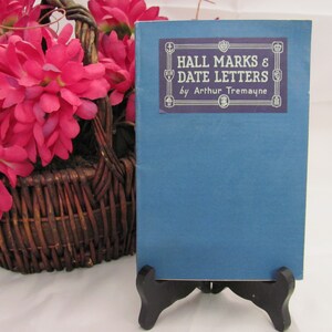 May include: A blue hardcover book titled "Hall Marks & Date Letters" by Arthur Tremayne. The book is on a black book stand.