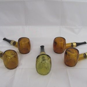 May include: Five glass bottles shaped like pipes, with brown and green glass. The bottles have a textured design and black stoppers.