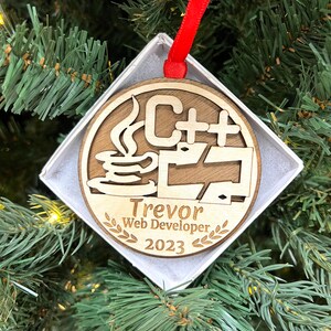 May include: A wooden Christmas ornament with a coffee cup and the text "C++" on it. The ornament also has the text "Trevor Web Developer 2023" on it.