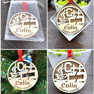 May include: A wooden Christmas ornament with a red ribbon. The ornament features a stylized image of a coffee cup with steam, a computer monitor, and the text "C++". The ornament also includes the name "Colin" in a decorative font.