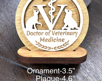 May include: Wooden plaque with a white circle featuring a stylized 'V' with a snake wrapped around it, a cat and a dog on either side, and the text 'Doctor of Veterinary Medicine'. The plaque is on a wooden stand. Ornament-3.5", Plaque-4.6", Wall sign-10.8", Large wall sign-14"