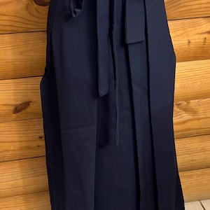 May include: A solid navy blue wrap skirt featuring a high-waisted design with a matching fabric tie belt at the waist. The skirt has a long, straight silhouette that falls below the knees, constructed from a smooth, opaque fabric material.