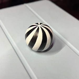 Puede incluir: Una esfera de rayas blancas y negras con un acabado brillante. La esfera está pintada con rayas blancas que irradian desde la parte superior.