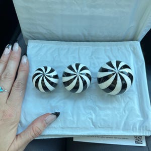 Może przedstawiać: Trzy ozdobne kule z czarno-białym spiralnym wzorem. Kule ułożone są na białej powierzchni. Kule mają różne rozmiary.