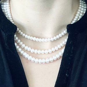 Può includere: Una collana di perle a più fili con perle bianche. La collana è indossata da una persona con una camicia nera.