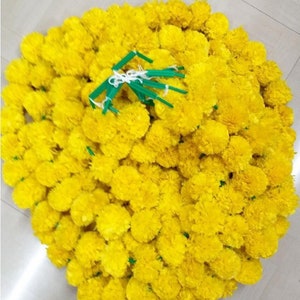 Puede incluir: Un gran mont&oacute;n de guirnaldas de flores de cal&eacute;ndula de color amarillo brillante. Las guirnaldas est&aacute;n hechas de seda y est&aacute;n atadas con cuerda verde.