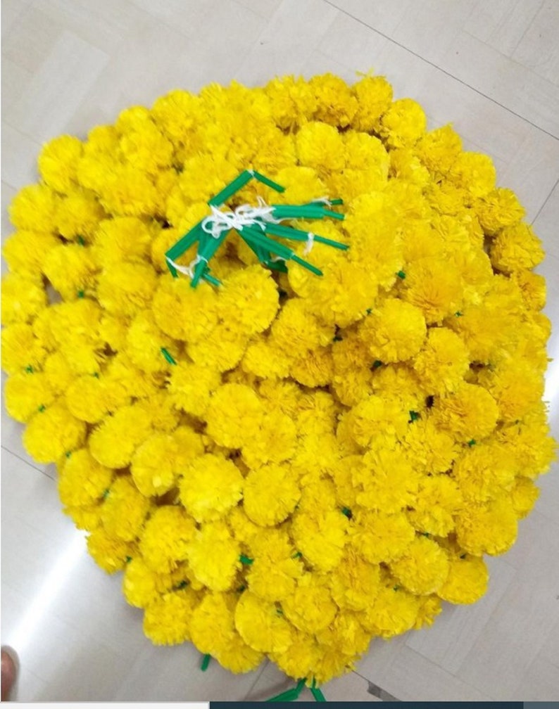Puede incluir: Un gran mont&oacute;n de guirnaldas de flores de cal&eacute;ndula de color amarillo brillante. Las guirnaldas est&aacute;n hechas de seda y est&aacute;n atadas con cuerda verde.