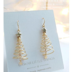 May include: Gold Christmas tree earrings with clear crystals and a gold star at the bottom. The earrings are on a white card with the text "CAWAII LITTLE THINGS Handmade Japanese craft".