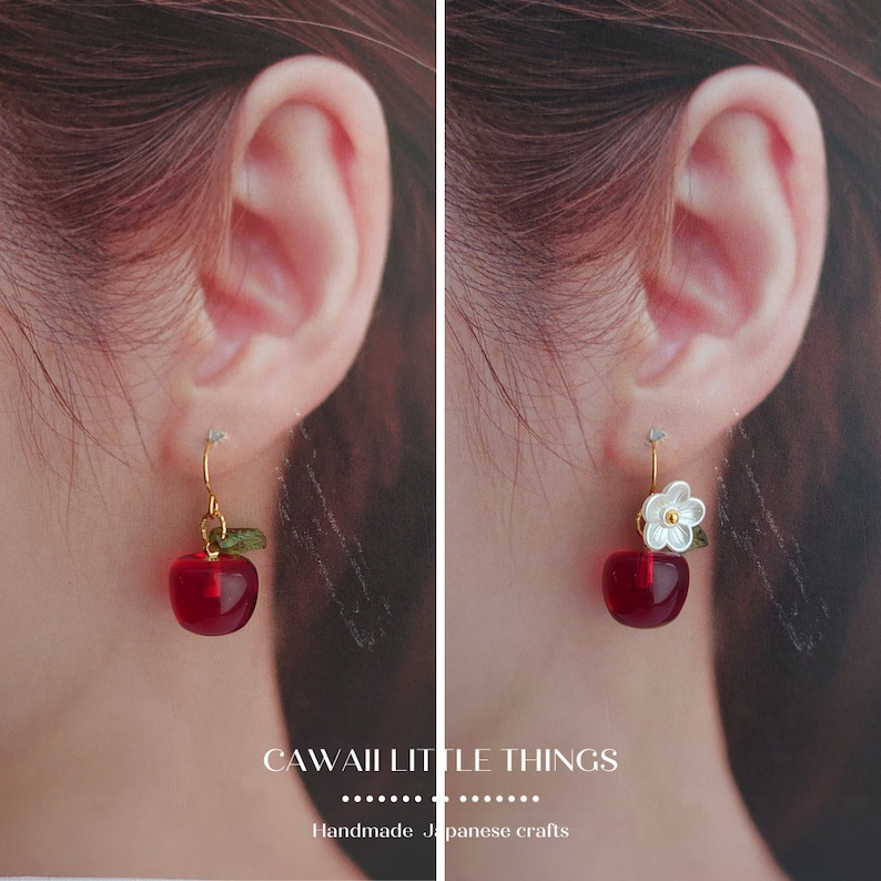 Puede incluir: Pendientes rojos en forma de manzana con ganchos dorados. Un pendiente tiene una peque&ntilde;a hoja verde y el otro una flor blanca con un centro dorado. El texto "CAWAII LITTLE THINGS" y "Handmade Japanese crafts" est&aacute; en la parte inferior.