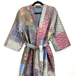 May include: A patchwork quilted robe with long sleeves and a sash tie. The robe is made from a variety of fabrics in shades of blue, green, pink, and brown. The fabric has a variety of patterns, including floral, geometric, and paisley.