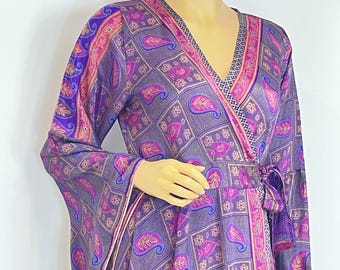 Peut inclure: Robe portefeuille à manches longues avec un motif cachemire violet et rose. La robe présente un col en V, une taille nouée et une jupe fluide. Le tissu est brillant et le motif comprend des éléments floraux et géométriques.